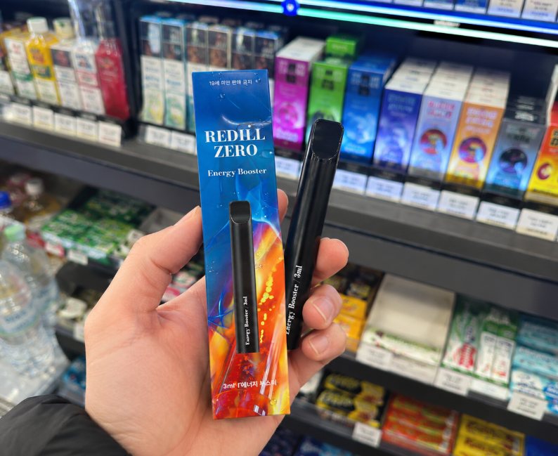 레딜 스틱 무니코틴 일회용 전자담배 3ml 에너지부스터 패키지를 편의점 매대 앞에서 든 모습
